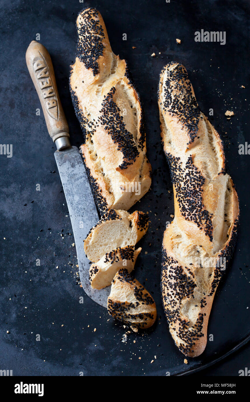 Due baguette con cumino nero e un coltello per pane su metallo scuro Foto Stock