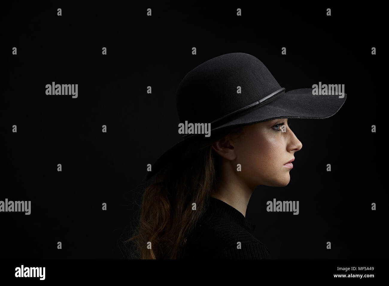 Profilo di triste giovane donna indossa cappello nero su sfondo nero Foto Stock