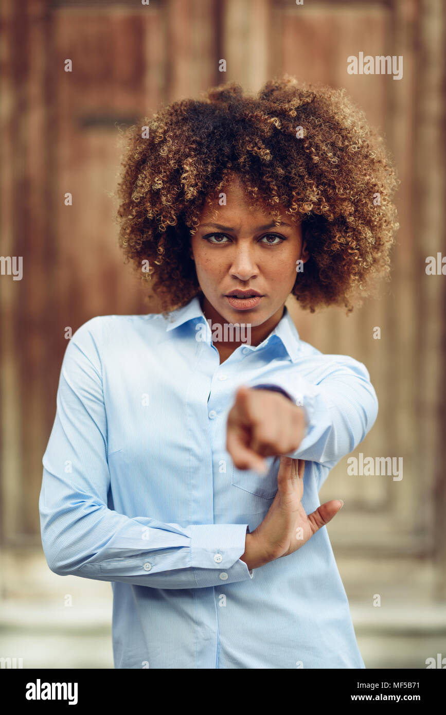 Spagna, Andalusia Malaga. Giovane donna nera, acconciatura afro, puntando con il dito in strada. Ragazza, modello di moda, indossare abiti casual in Foto Stock
