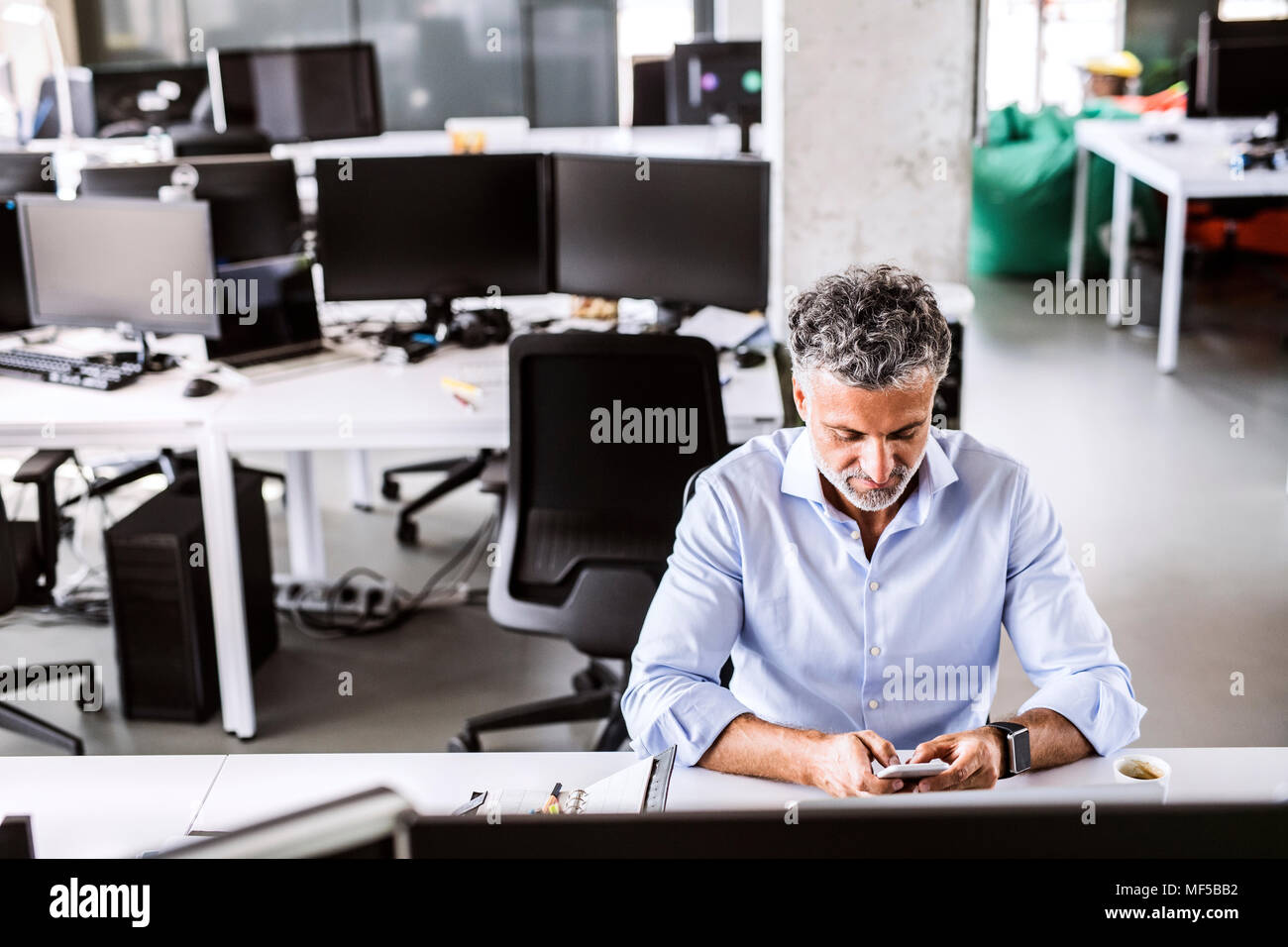 Imprenditore maturo seduto alla scrivania in ufficio utilizza lo smartphone Foto Stock