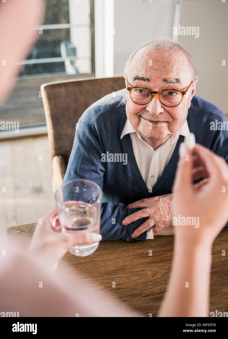 Donna che mantiene la pillola e bicchiere di acqua per sorridente uomo senior Foto Stock
