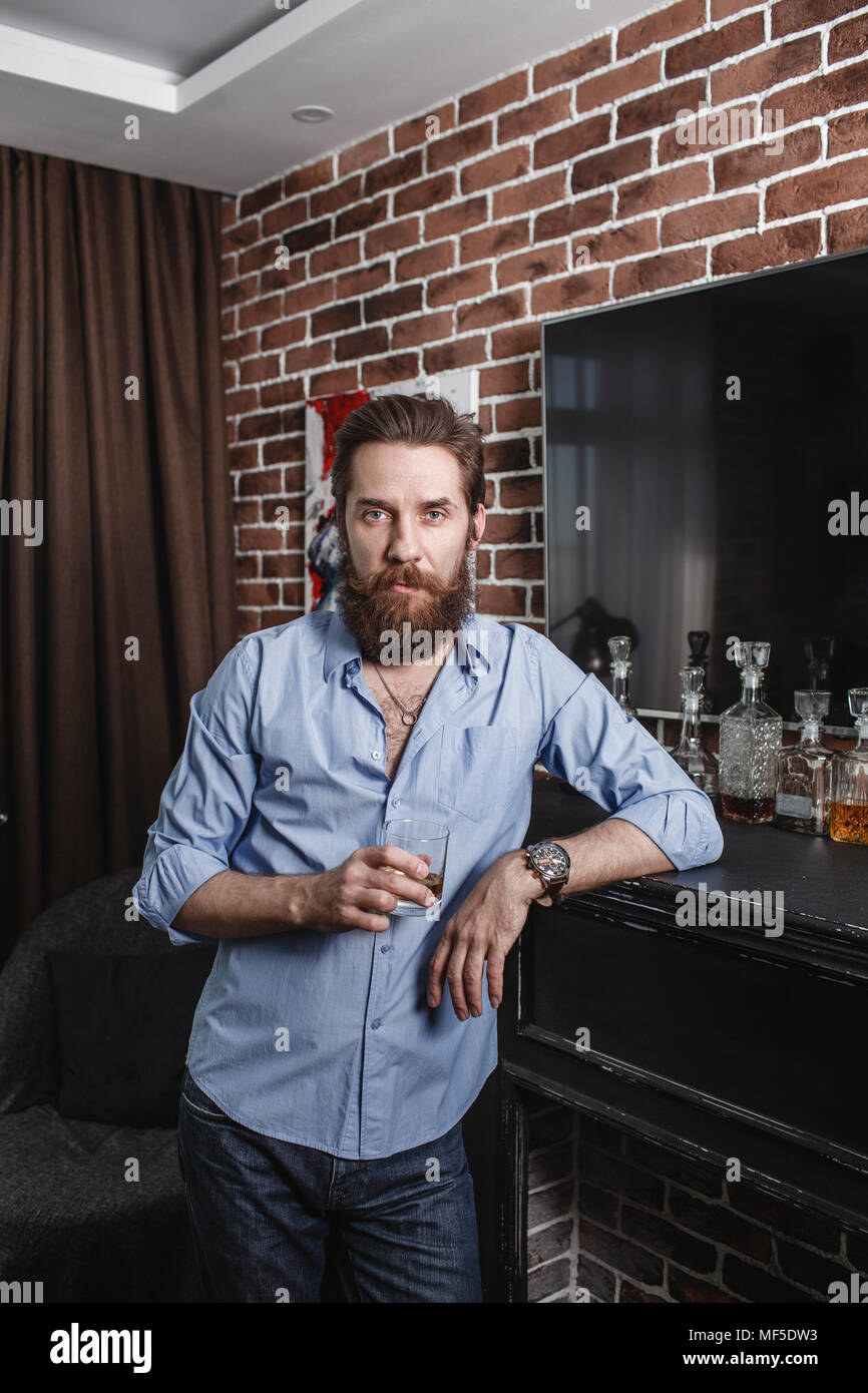 Ritratto di uomo barbuto con un bicchiere di whiskey a casa Foto Stock