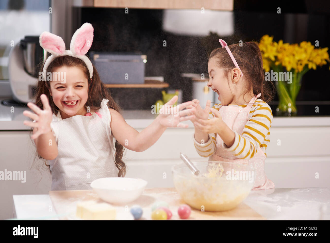 Due sorelle giocoso divertimento cottura biscotti di Pasqua in cucina insieme Foto Stock