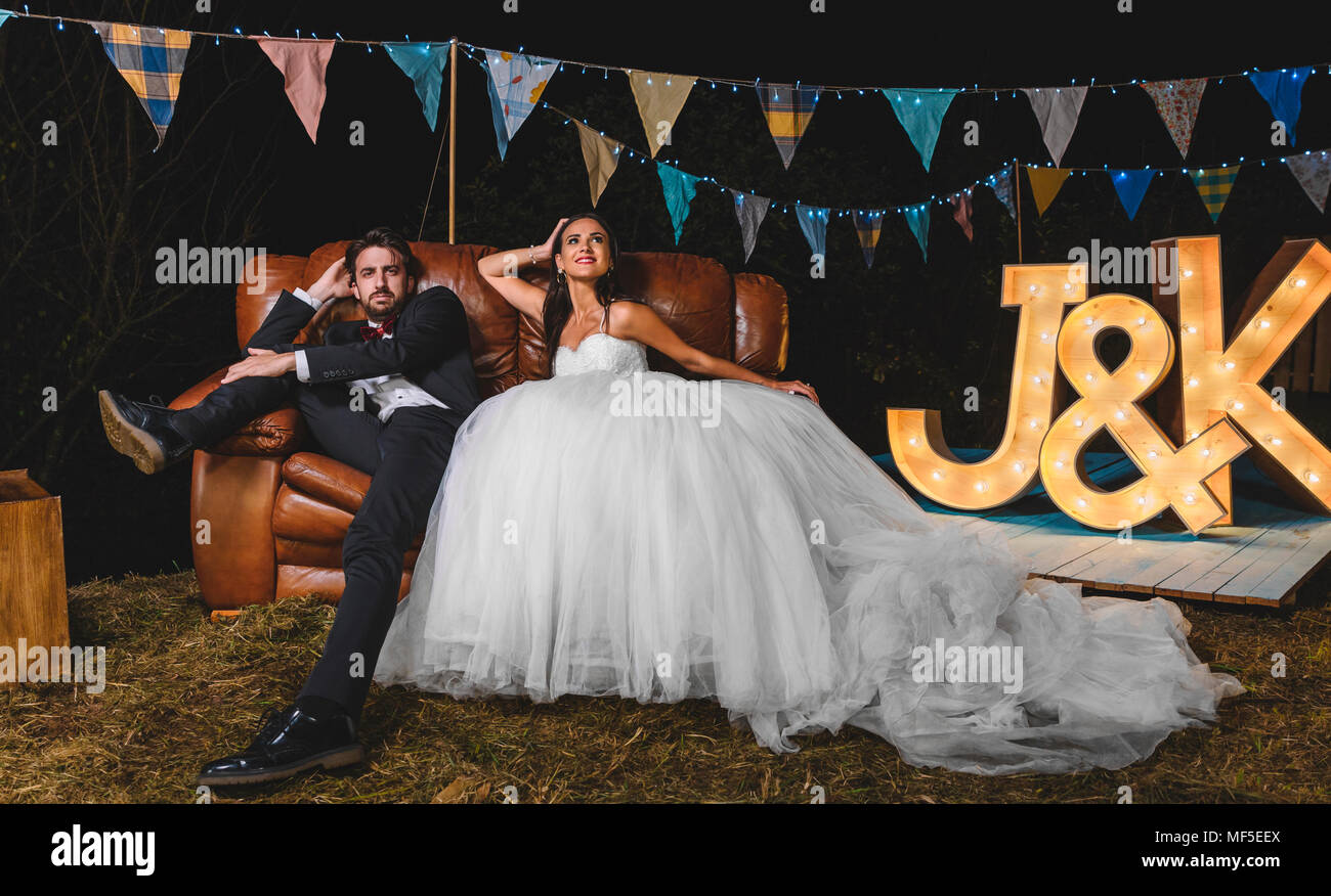 Ritratto di coppie in viaggio di nozze in posa seduta sul divano su un campo di notte party Foto Stock