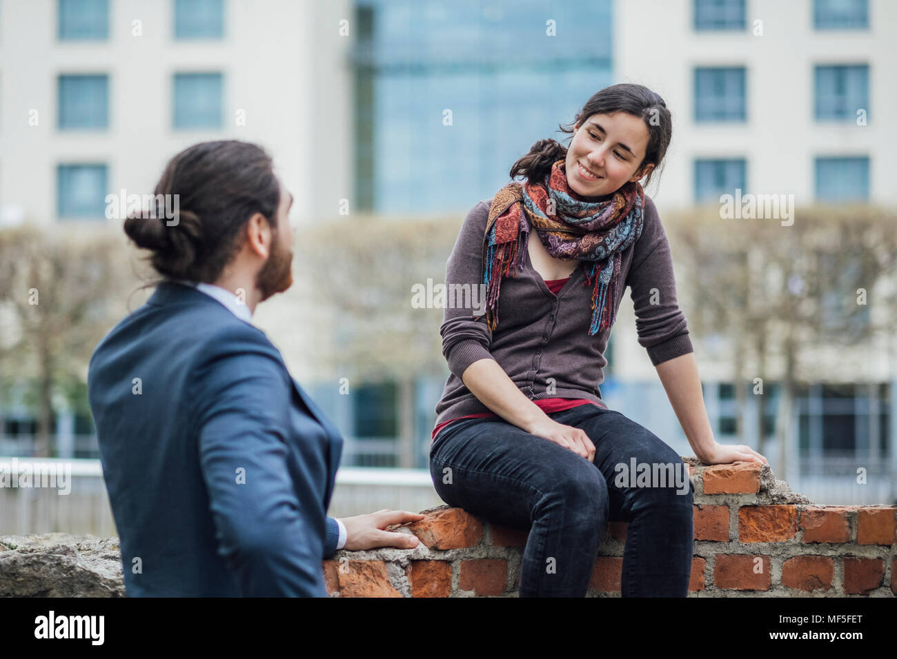Donna seduta su un muro fuori ufficio edificio sorridente a imprenditore Foto Stock