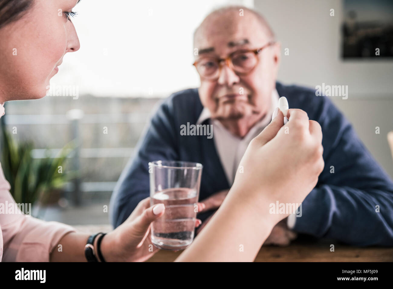 Donna che mantiene la pillola e bicchiere di acqua per uomo senior Foto Stock
