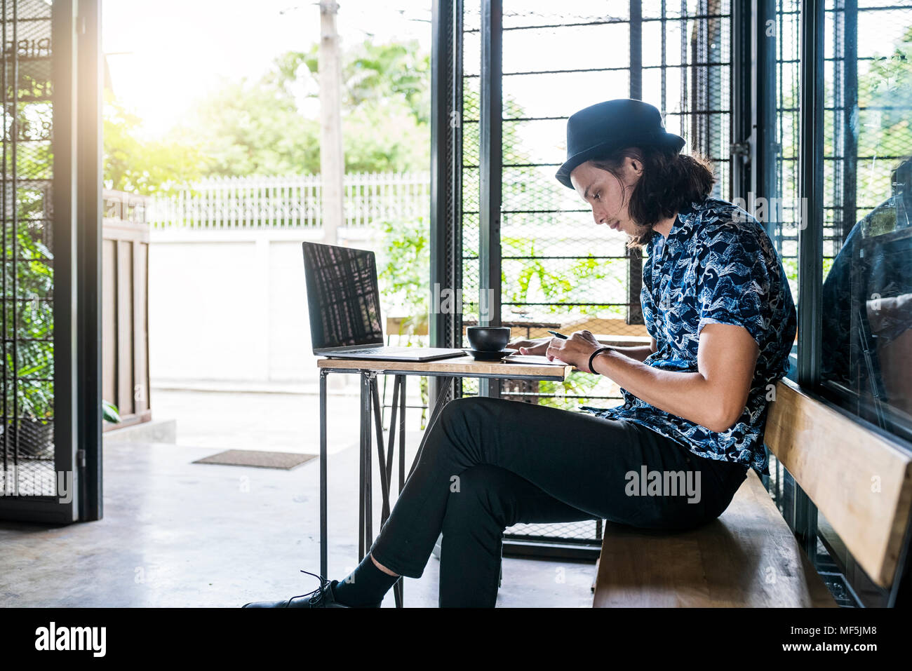 Artista di scrivere nel notebook in una caffetteria con caffè e il computer portatile sul tavolo Foto Stock