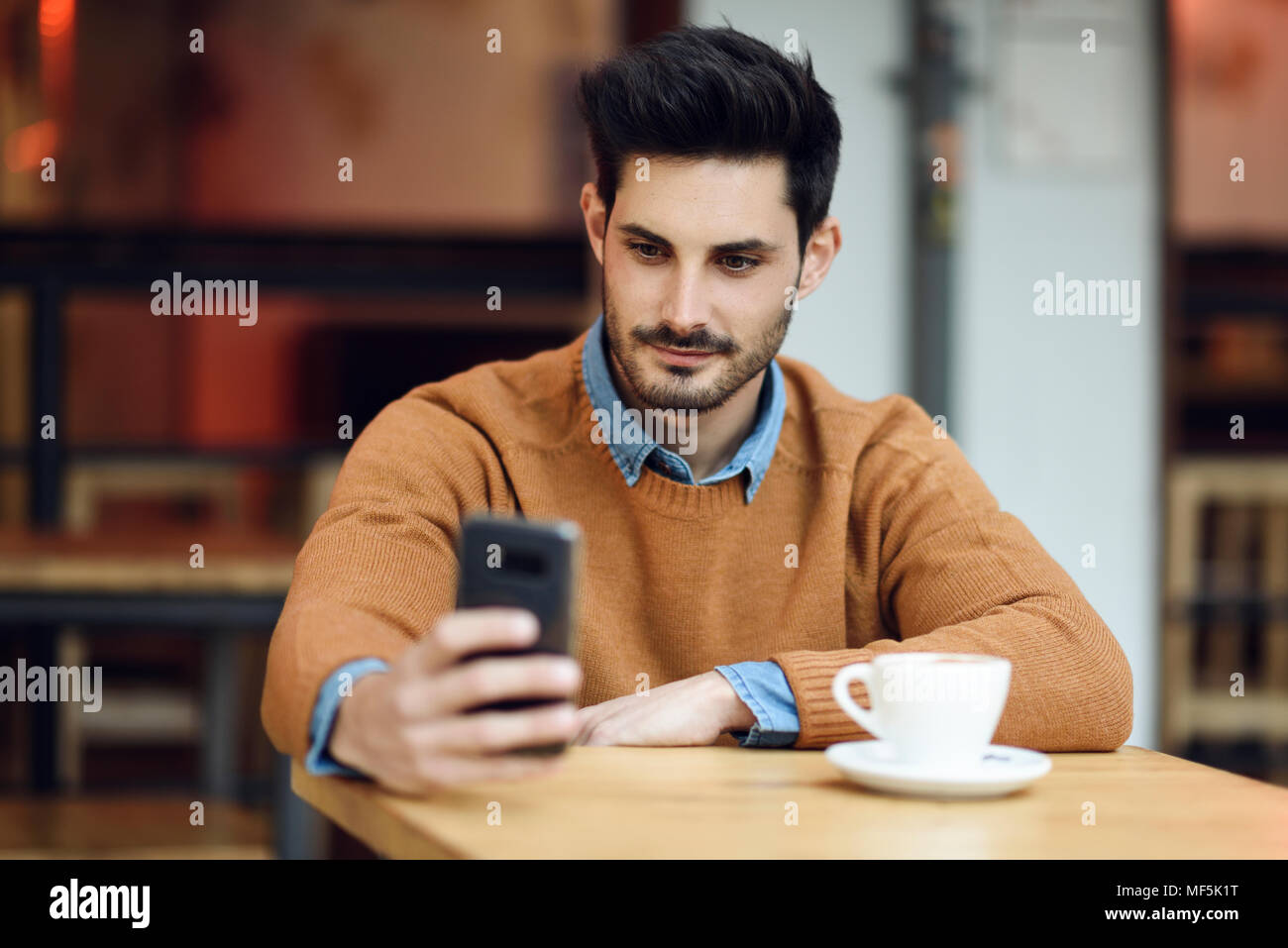 Spagna, Andalusia, Granada. Attraente giovane con moderni acconciatura seduto in un bar caffetteria guardando il suo smart phone. Il concetto di stile di vita. Foto Stock
