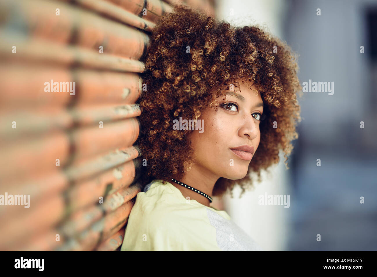 Spagna, Andalusia Malaga. Giovane donna nera, acconciatura afro guardando lontano in strada urbana di indossare un abbigliamento informale. I giovani uno stile di vita urbano. Foto Stock