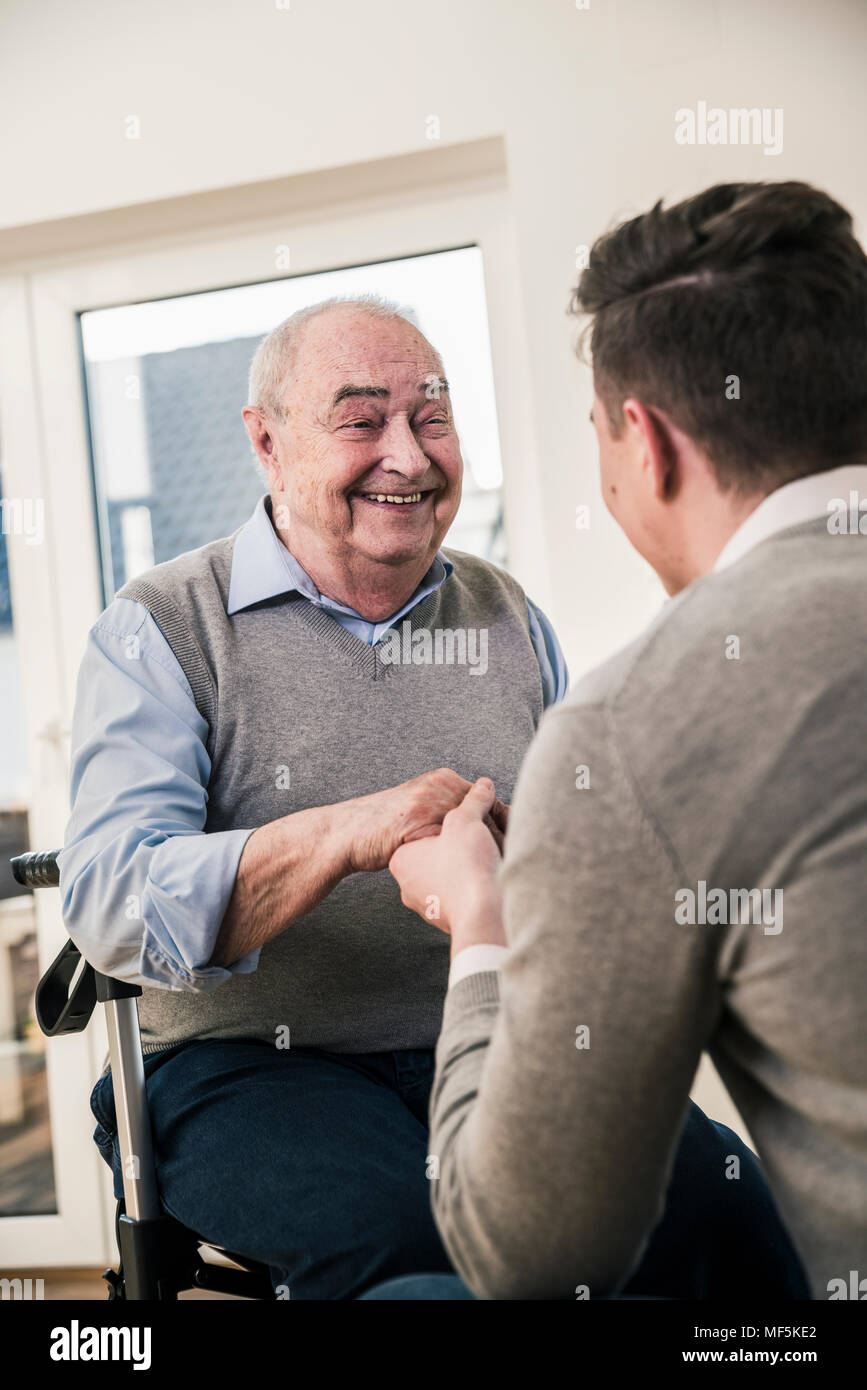 Senior uomo sorridente al giovane uomo tiene le mani Foto Stock