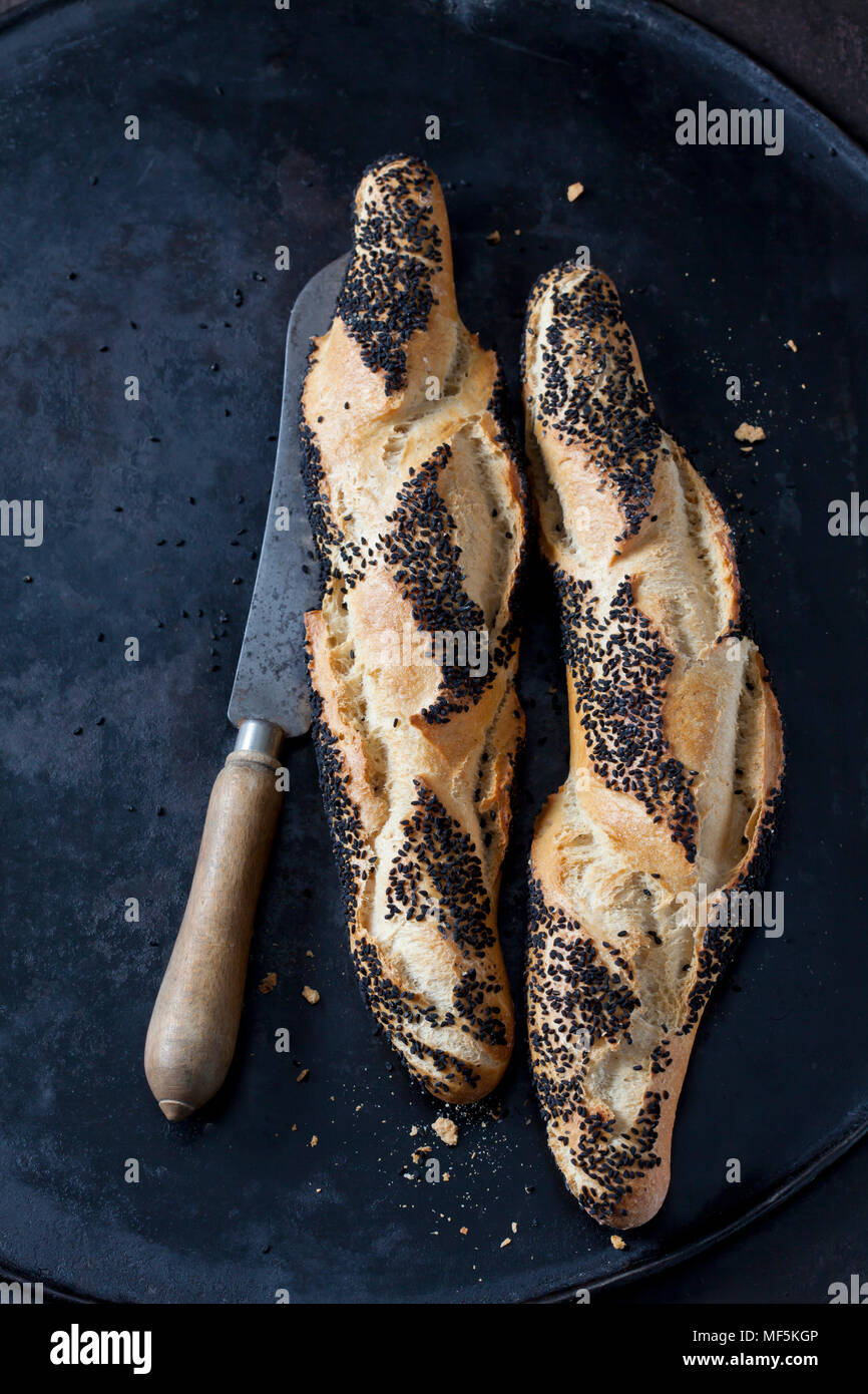 Due baguette con cumino nero e un coltello per pane su metallo scuro Foto Stock
