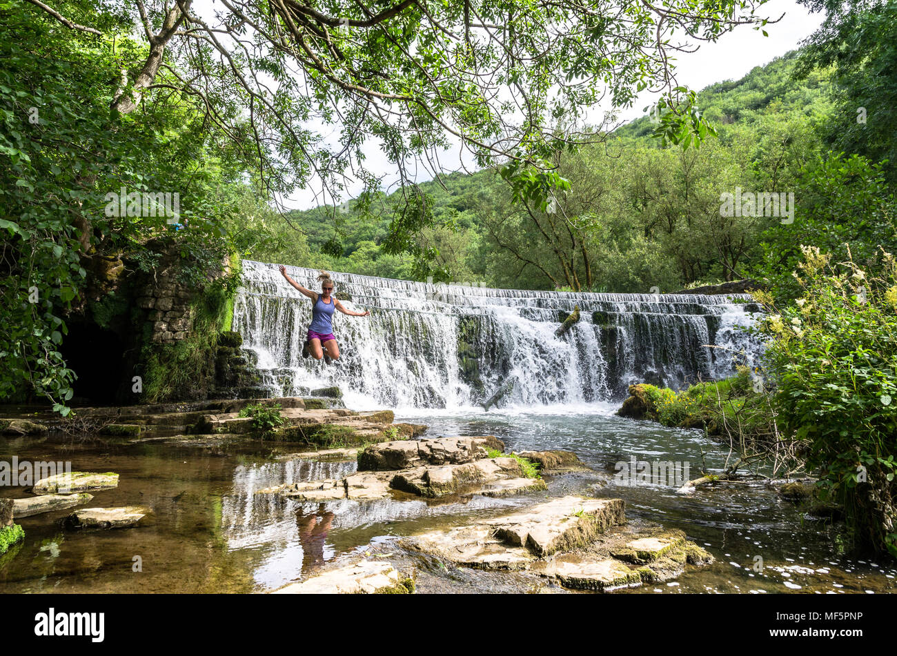 Una giovane donna salti di gioia da una cascata nel bosco. Foto Stock