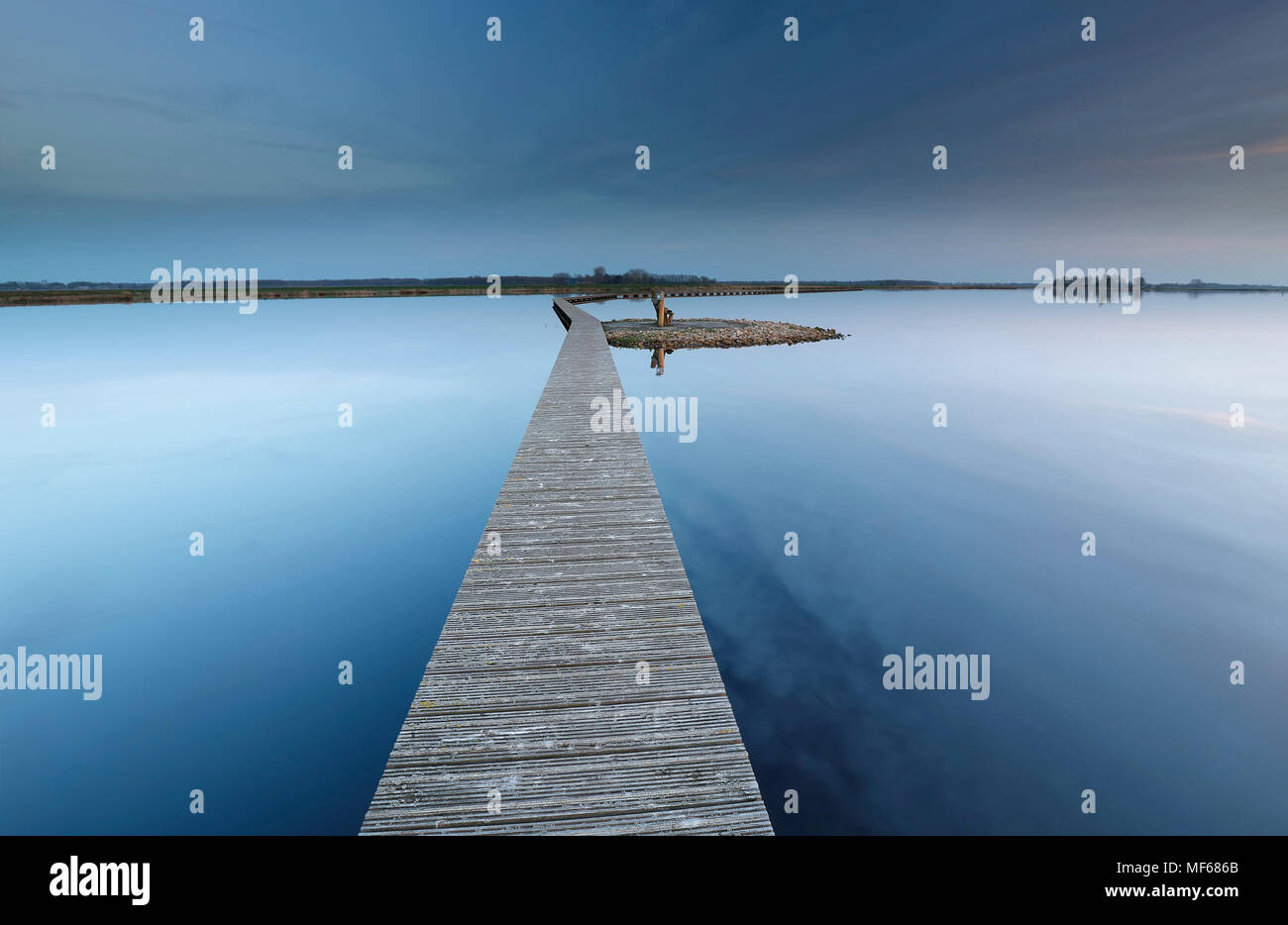 Passerella in legno su acqua ad isola con banco nel crepuscolo Foto Stock