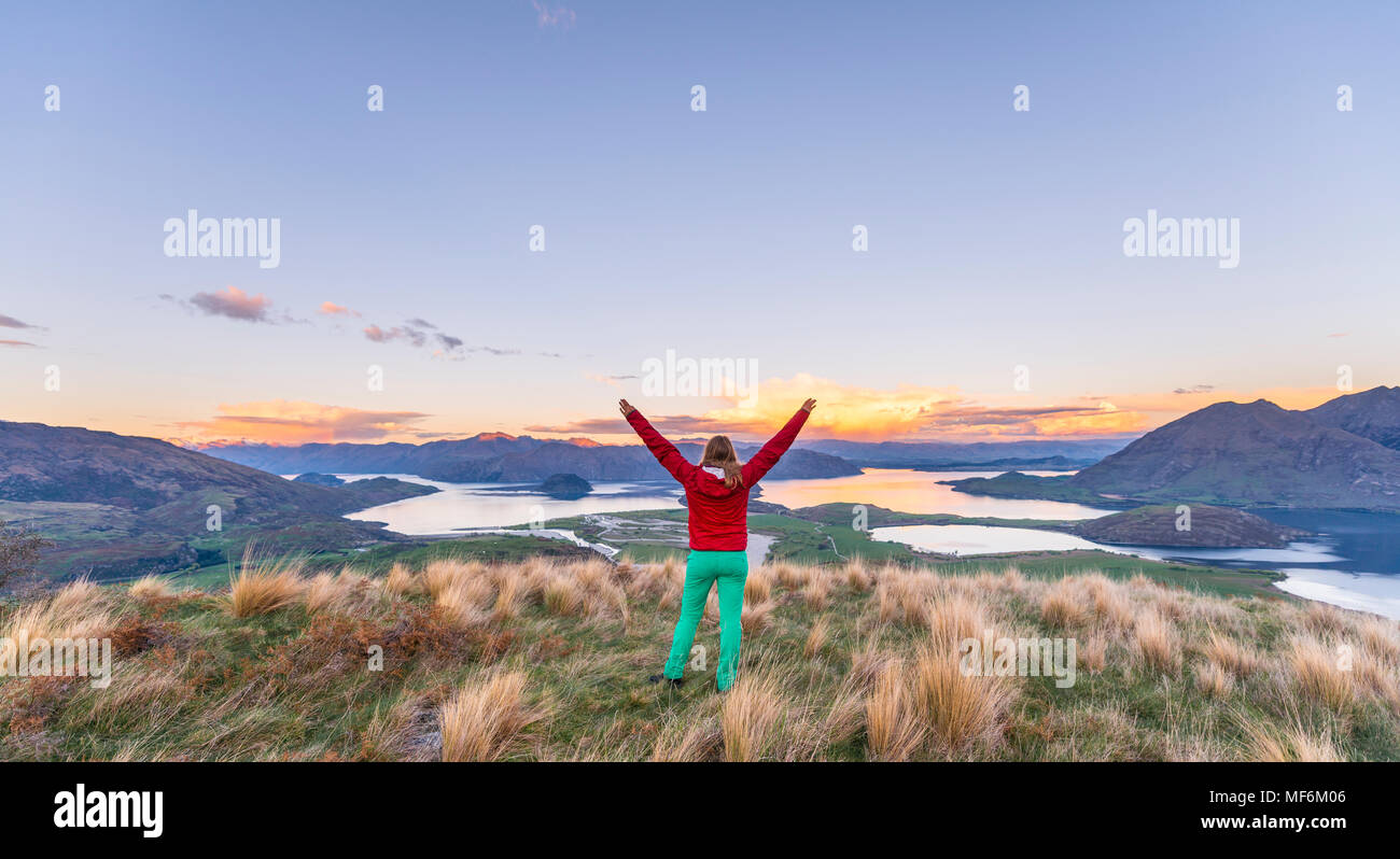 Escursionista con le braccia distese in aria, la vista del Lago Wanaka e montagne, tramonto, picco roccioso, Glendhu Bay, Otago Southland Foto Stock