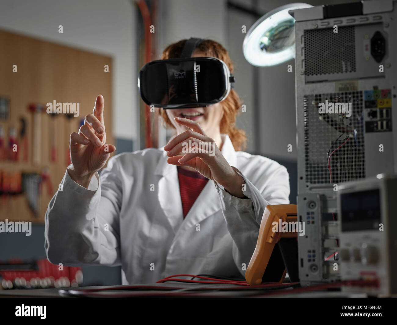 Donna con occhiali VR e camice seduto in un laboratorio di elettronica, Austria Foto Stock