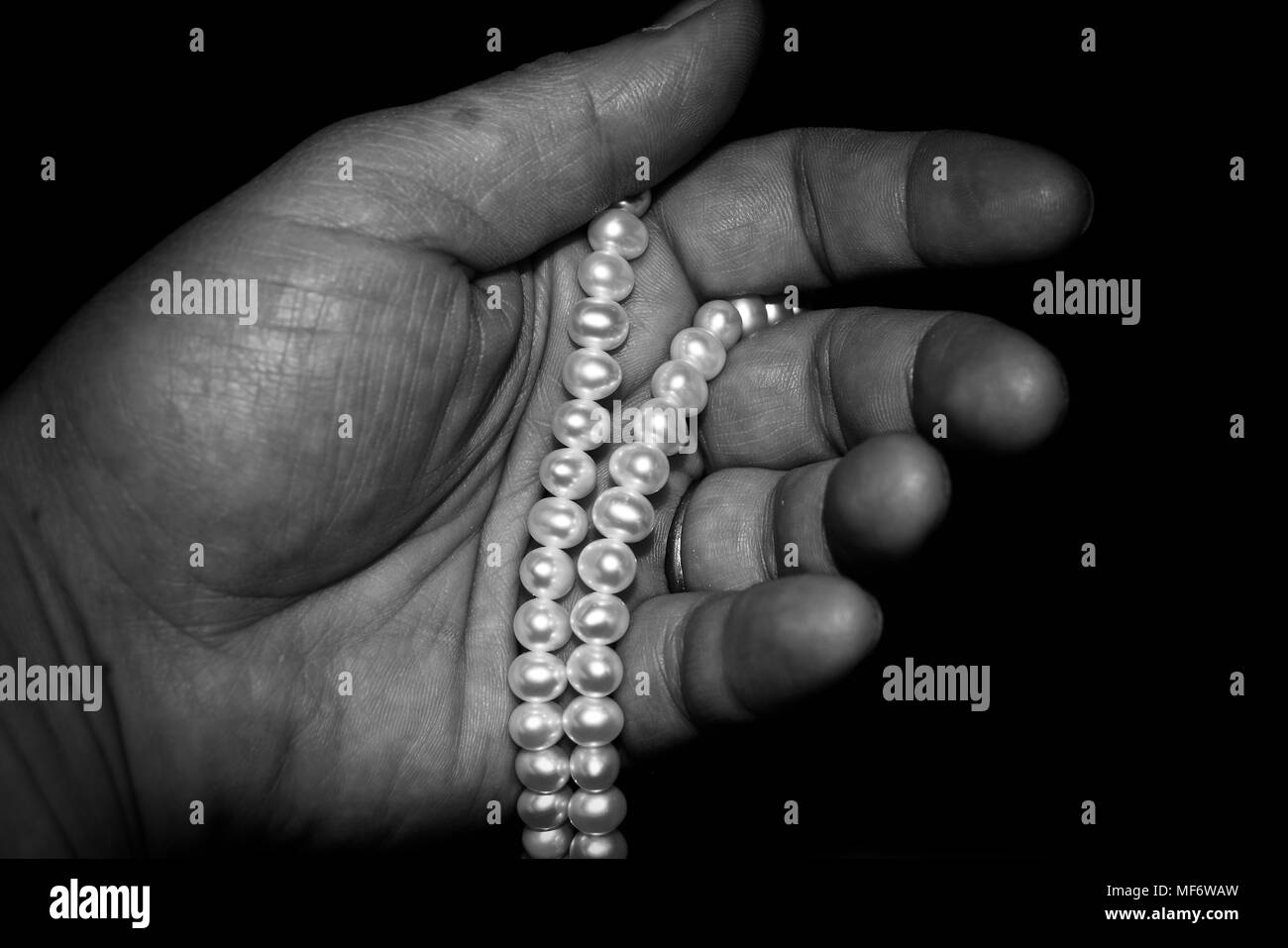 Un unico centro donna più anziana mano che tiene una collana di perl.sfondo è nero. Foto in bianco e nero. Foto Stock