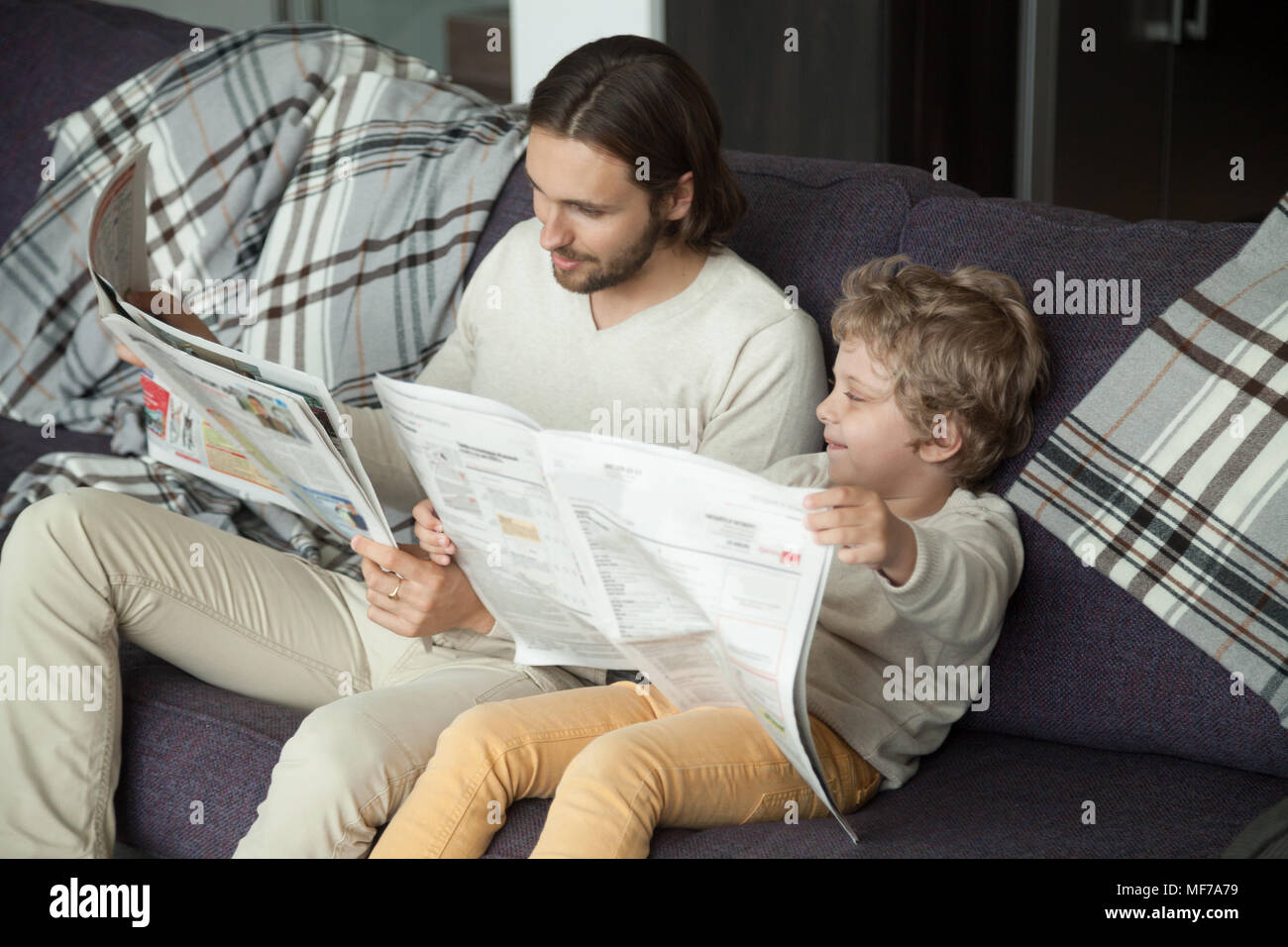 Carino kid figlio leggendo il giornale seduto sul divano con il papà Foto Stock