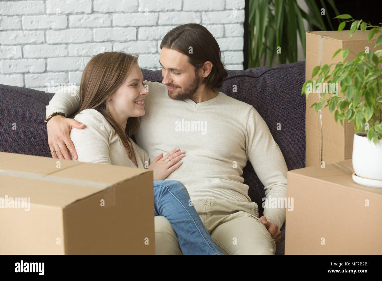 I noleggiatori sorridente abbracciando sul lettino nella nuova casa con scatole Foto Stock