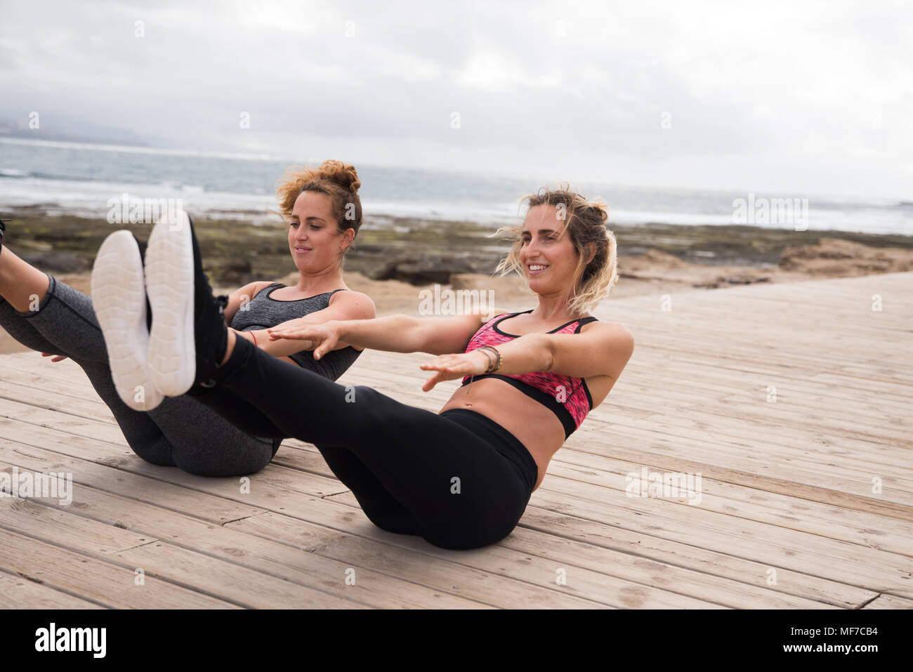 Due ragazze facendo esercizi addominali esterno sul Boardwalk in abbigliamento fitness Foto Stock