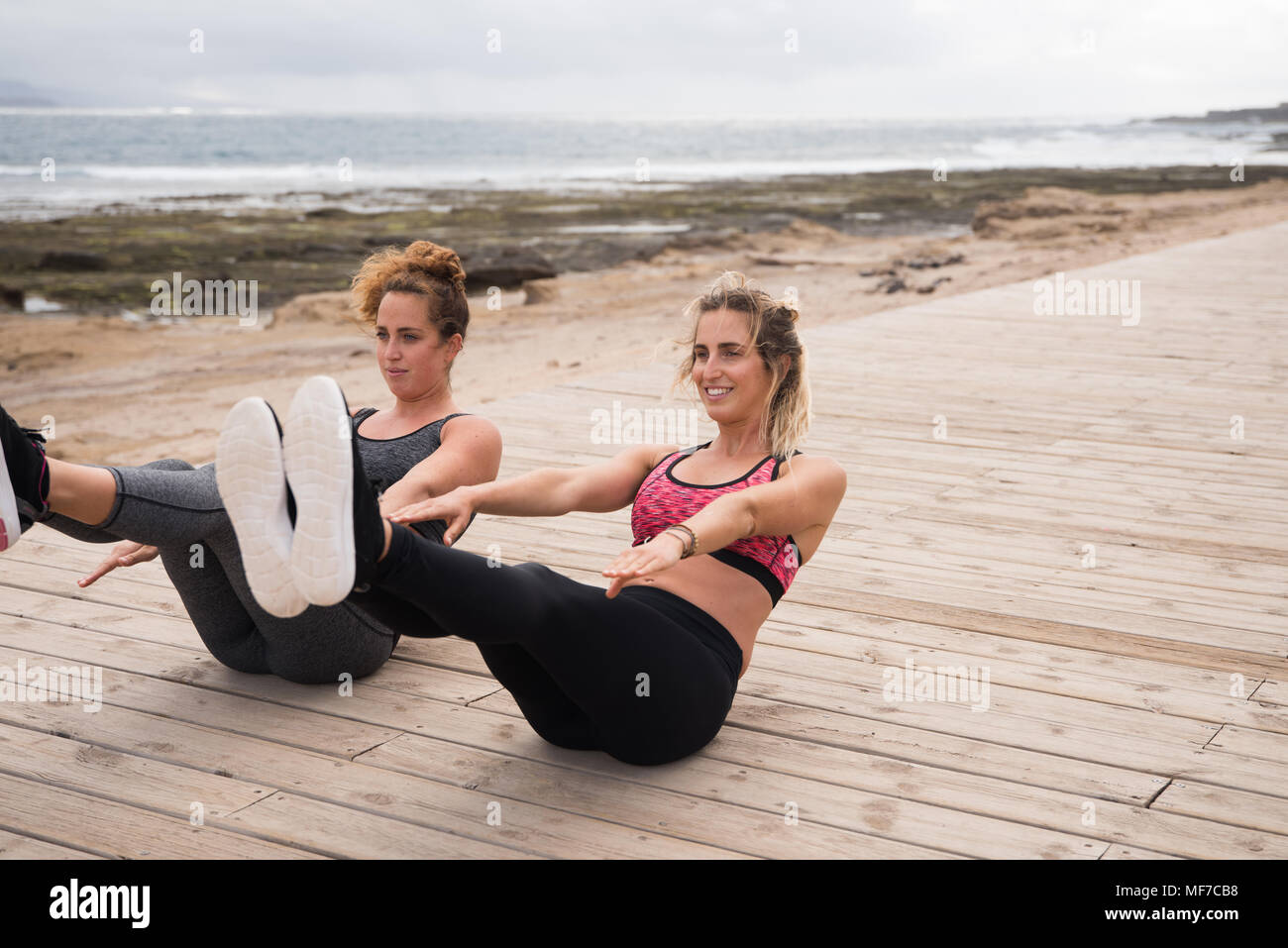 Giovani belle ragazze facendo un allenamento fitness esterno vicino al mare indossando sport collant e cime e solleva le gambe Foto Stock