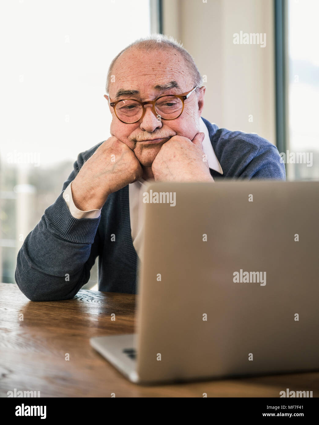 Senior uomo seduto a tavola guardando al laptop Foto Stock