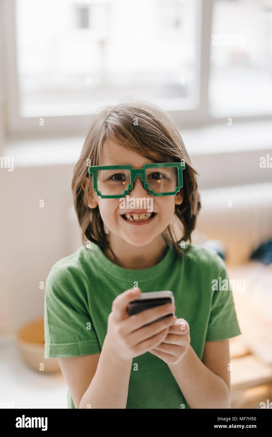 Ritratto di ragazzo sorridente indossando occhiali di pixel tenendo il telefono cellulare Foto Stock