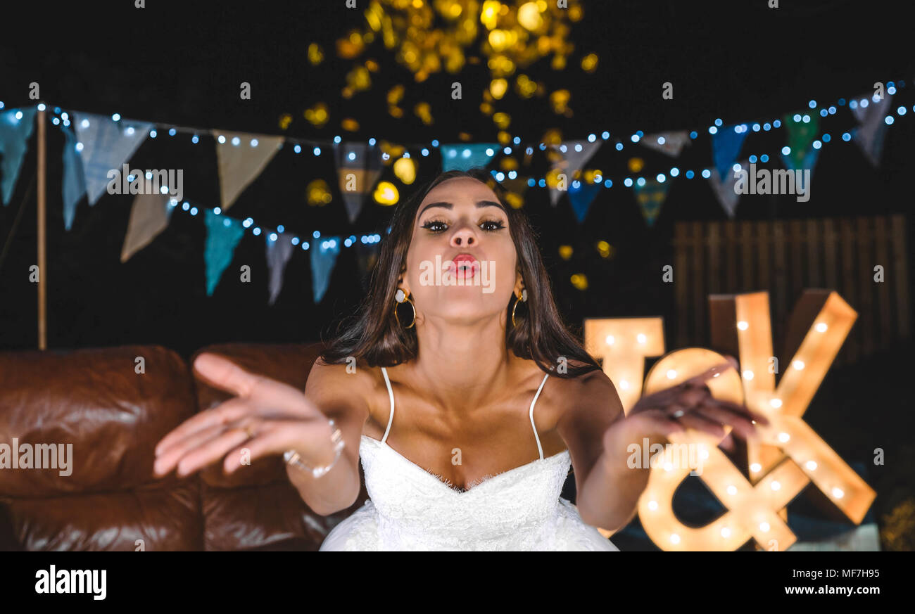 Ritratto di sposa felice soffiando coriandoli su una festa notturna all'aperto Foto Stock