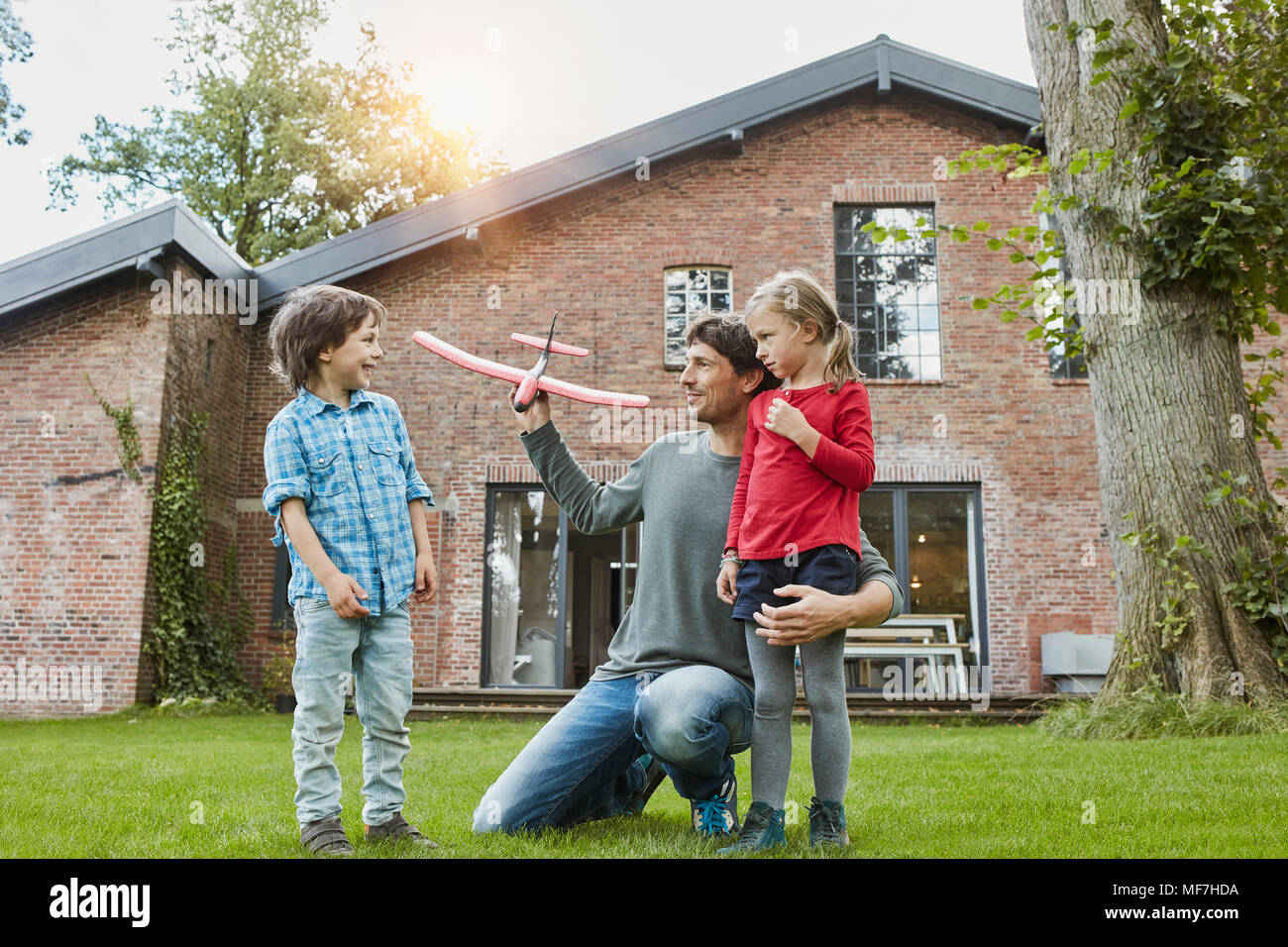 Padre di due bambini che giocano con aeroplano giocattolo nel giardino della loro casa Foto Stock