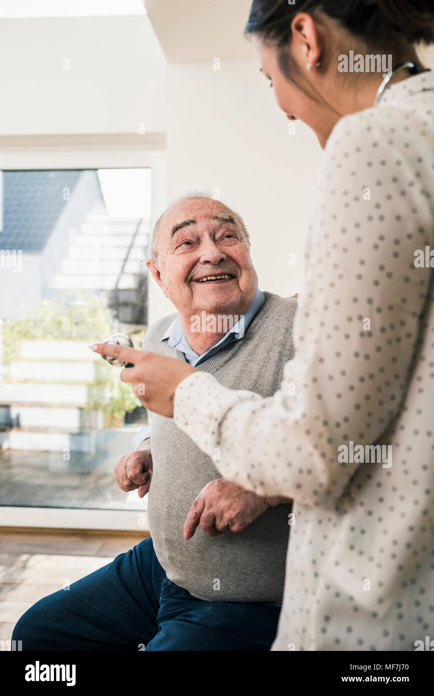 Senior uomo sorridente in un infermiere con uno stetoscopio a casa Foto Stock