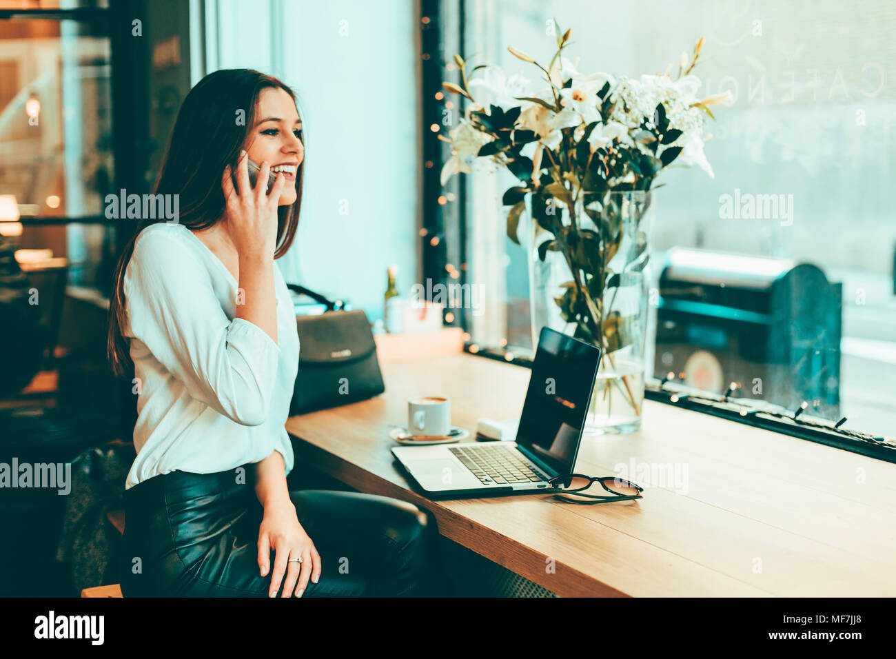 Felice giovane imprenditrice sul telefono in un coffee shop Foto Stock