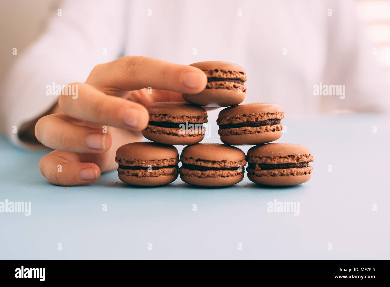 Donna immissione macarons sul mucchio sul tavolo blu. Messa a fuoco selettiva Foto Stock Donna immissione macarons sul mucchio sul tavolo blu. Messa a fuoco selettiva Foto Stock