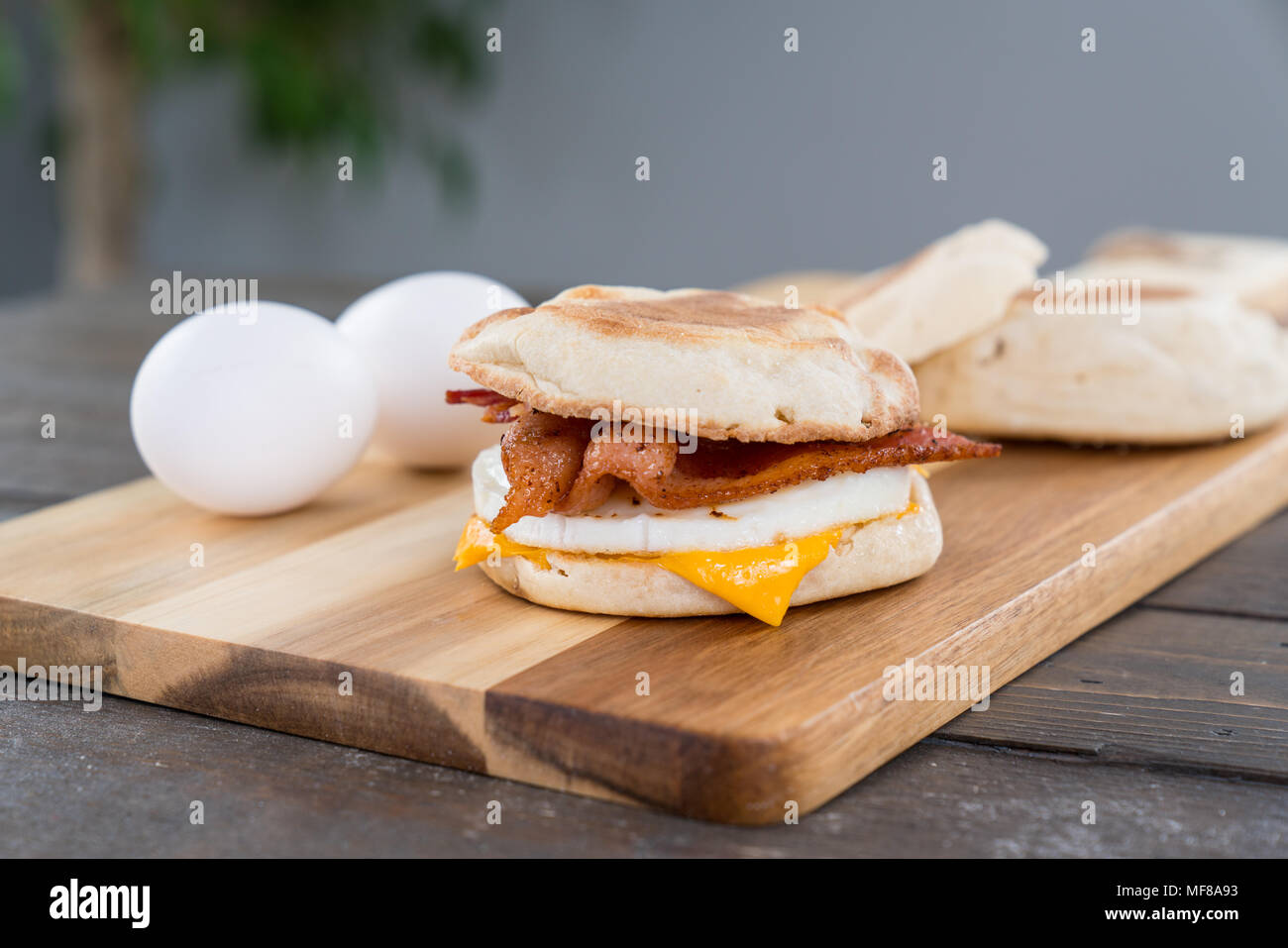 Bacon, uova e formaggio colazione panino con muffin inglese sul bordo di taglio Foto Stock