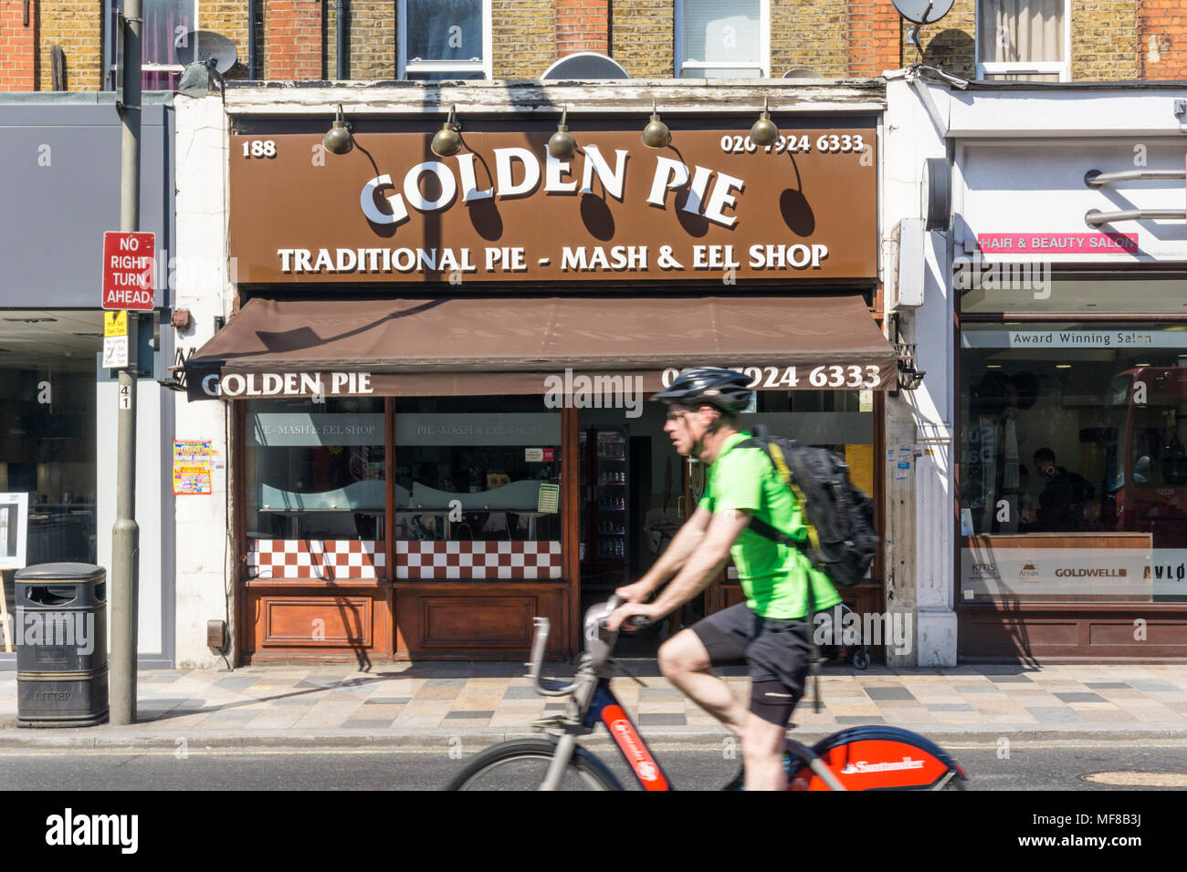 Ciclista, movimento sfocato, in sella a una moto di Santander passato il Golden Torta tradizionale & Mash eel pie shop a Clapham Junction. Foto Stock