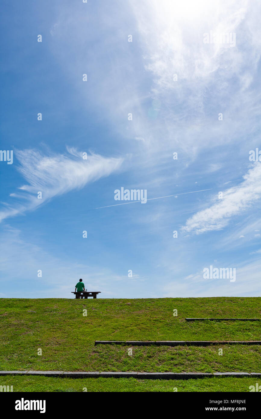 L'uomo da solo si siede sul sedile a panca sulla prateria, le nuvole di  cirro, il cielo blu sullo sfondo, Jialulan, Taiwan. Speranza, relax,  solitudine e amore concetto astratto Foto stock -