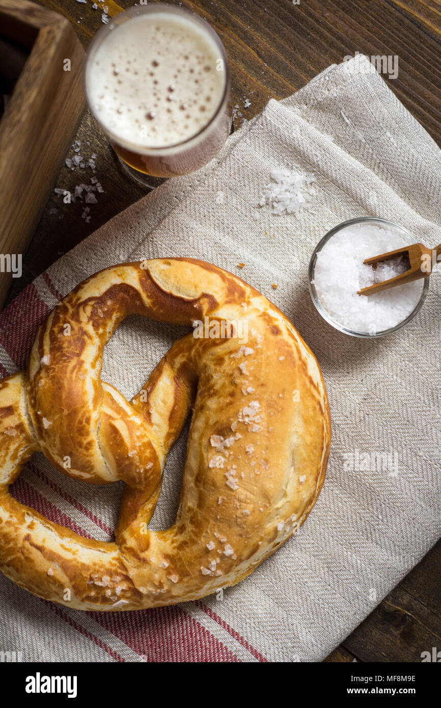 In casa Pretzel con sale marino e bicchiere di birra su tavola in legno rustico Foto Stock