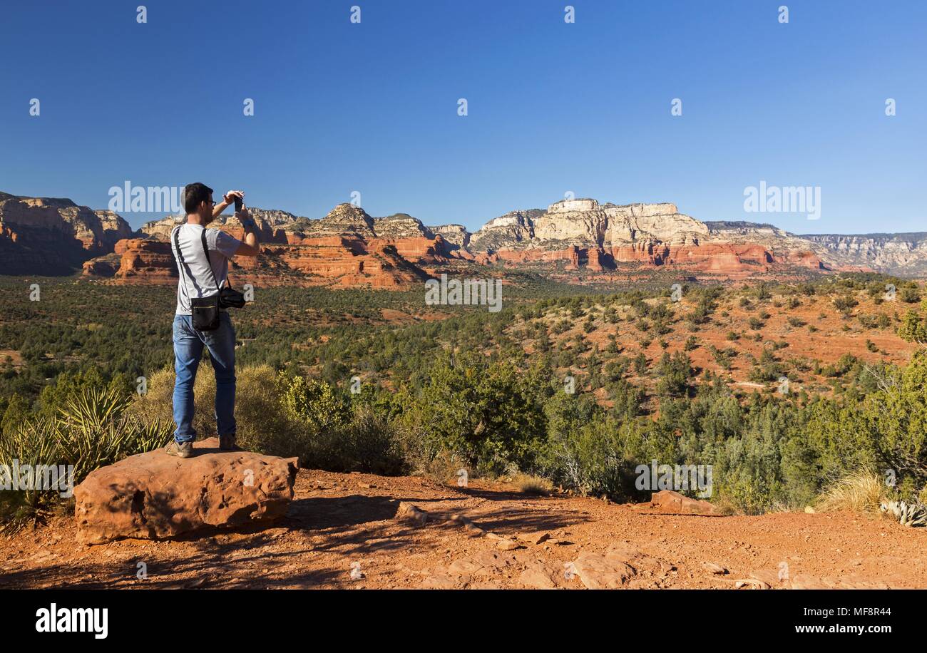 Giovane Maschio atletico a fotografare il paesaggio del deserto sul Ponte del Diavolo Sentiero escursionistico vicino a Sedona in Arizona sulla soleggiata giornata invernale Foto Stock