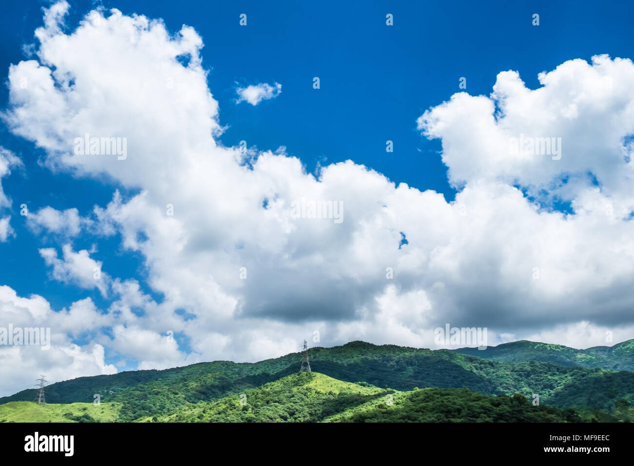 Il Cumulus bianche nuvole che sovrastano la montagna. Hing di tensione linea di alimentazione con energia elettrica tralicci passando attraverso le montagne. Foto Stock