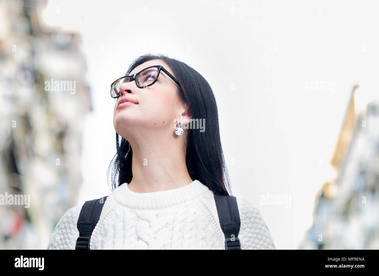 Attraente giovane singolo brunette girl tourist camminando per strada. La riflessione di luci della città nel suo bicchieri. Edifici sfocata sullo sfondo. Foto Stock