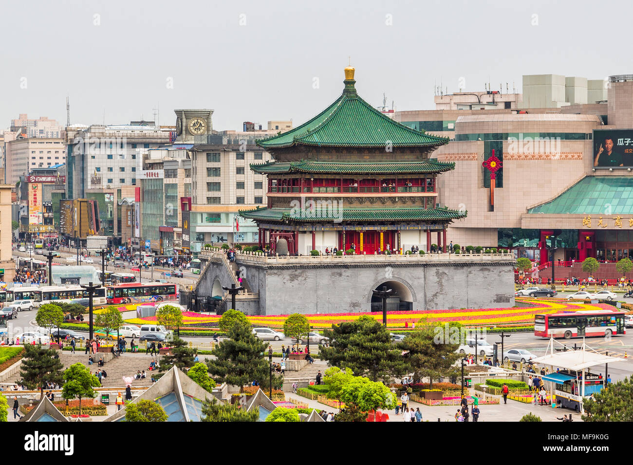 Xi'an torre campanaria con esso è ornato verde tetto di tegole si erge nel mezzo di un traffico occupato isola. Dietro di esso alcuni dei molti centri commerciali per lo shopping. Foto Stock