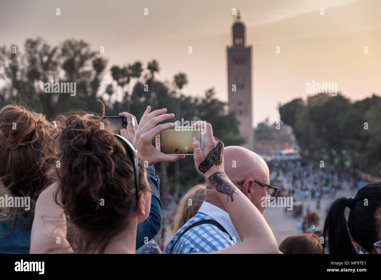 Una donna con Henna Tattoos su ther mani le fotografie la Moschea di Koutoubia sul suo iphone al tramonto, Marrakech, Marocco Foto Stock