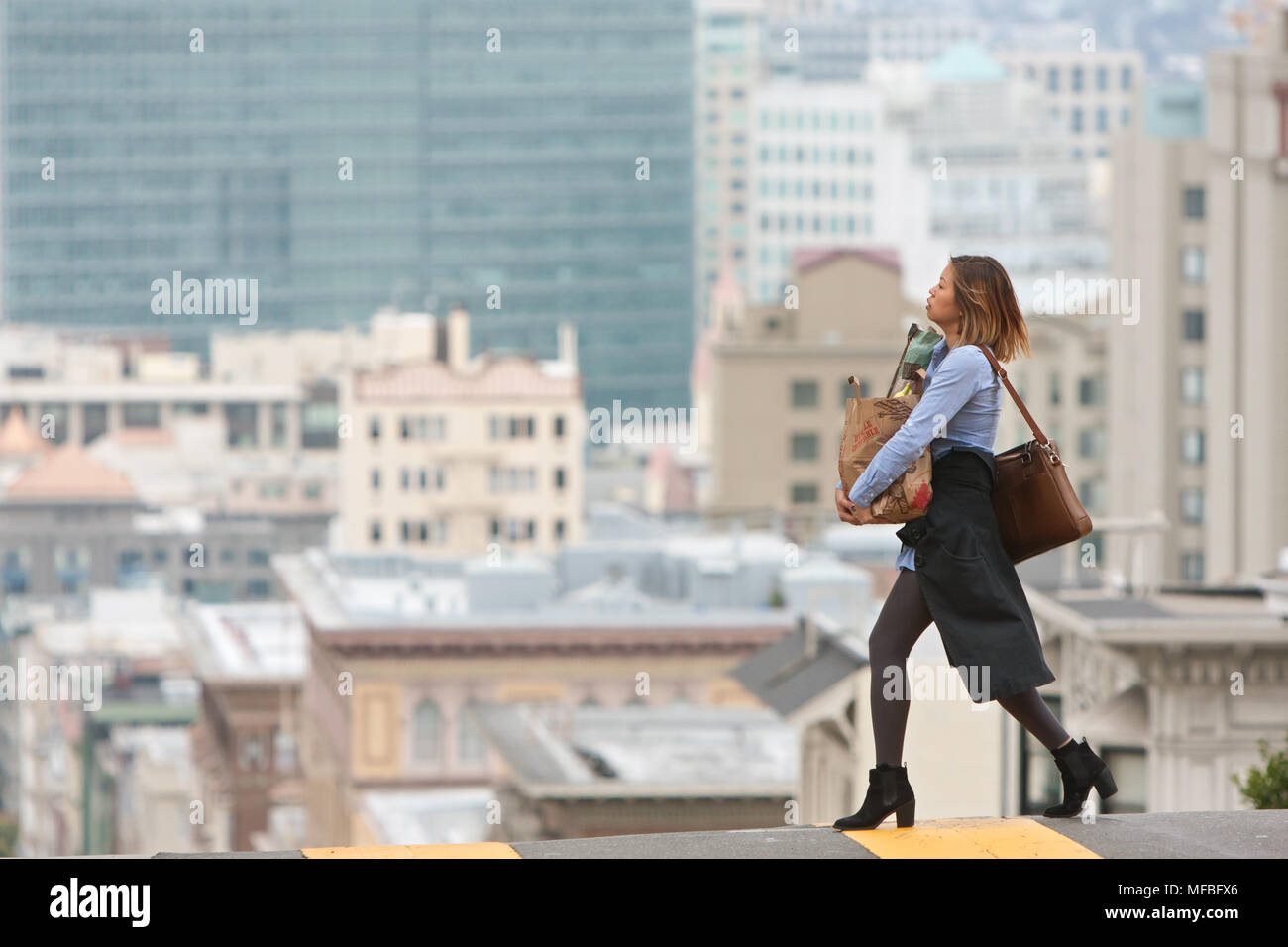 Un giovane, moda donna porta un sacco di negozi di generi alimentari al di là della strada in una elevata area di elevata nei pressi di Nob Hill, il 18 maggio 2015 a San Francisco, CA. Foto Stock