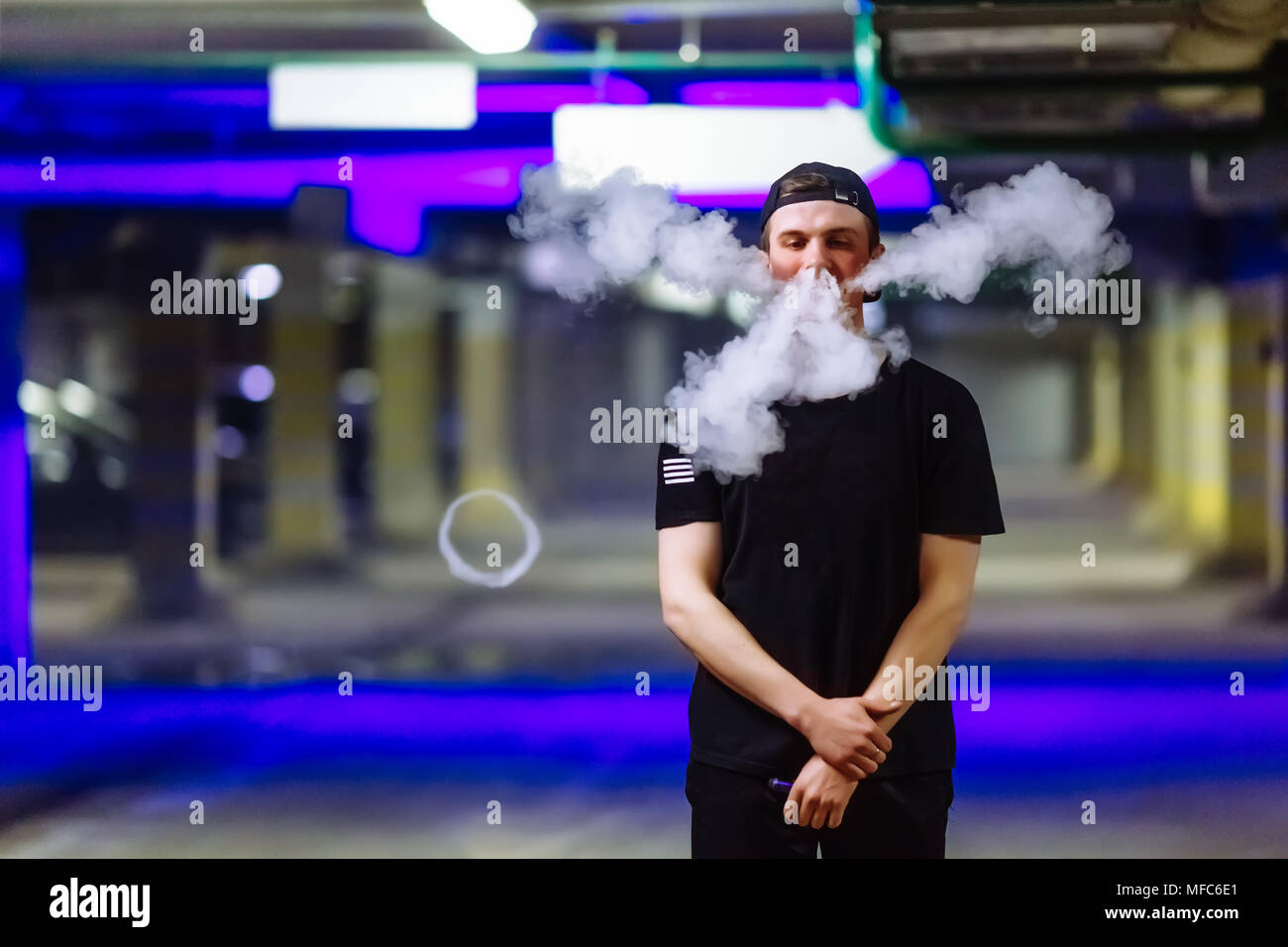 L uomo nel tappo un fumo di sigaretta elettronica e rilascia le nubi di vapore di eseguire vari tipi di vaping trucchi Foto Stock