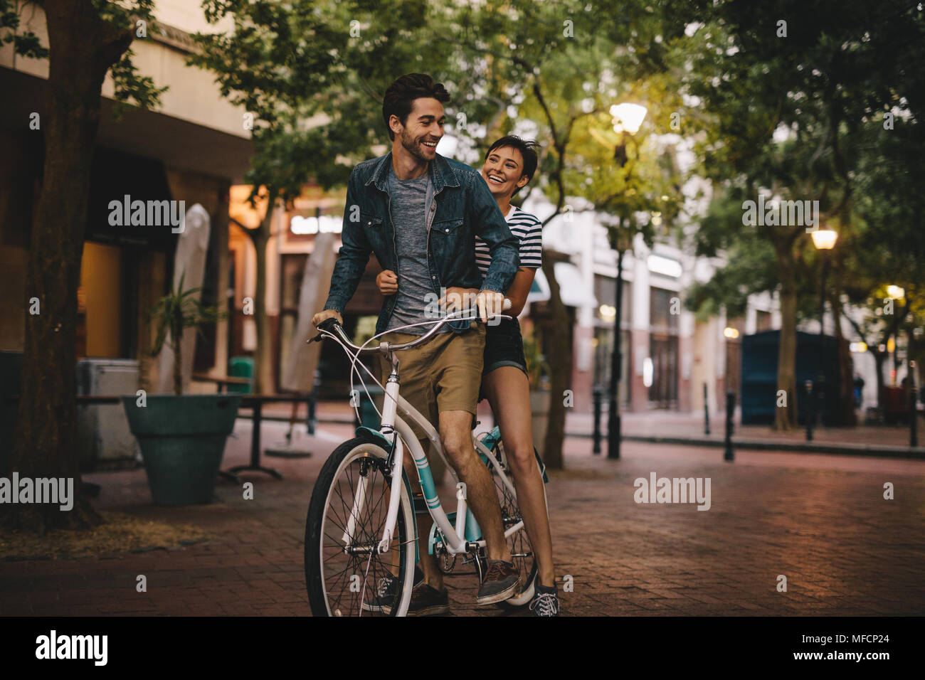 Amare giovane equitazione bicicletta sulla strada della città. Uomo Bicicletta Equitazione con la sua ragazza seduta in backseat. Foto Stock