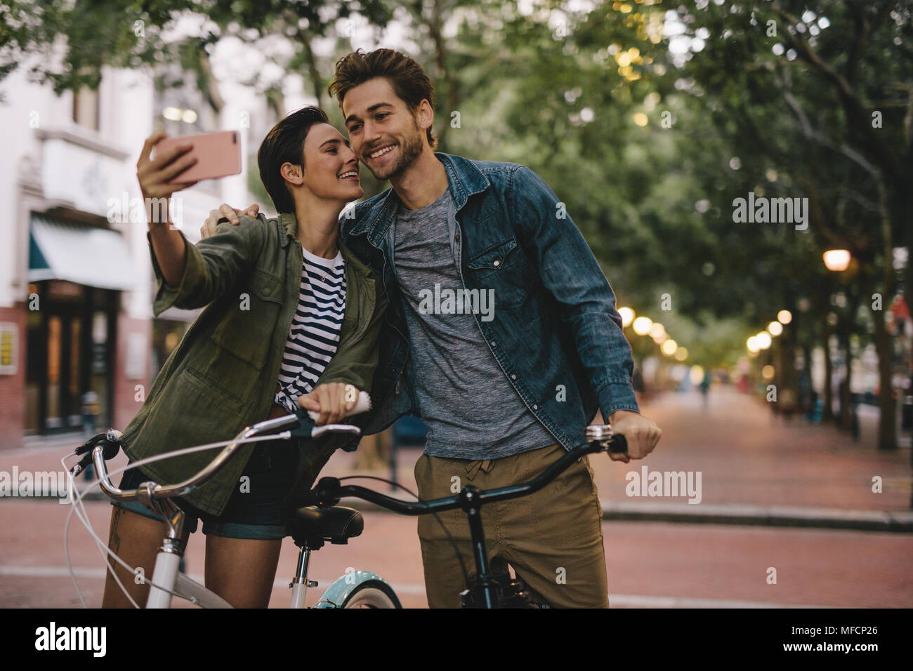 Coppia romantica con le biciclette tenendo selfie. Le donne che prendono selfie e la bacia fidanzati guancia. Foto Stock