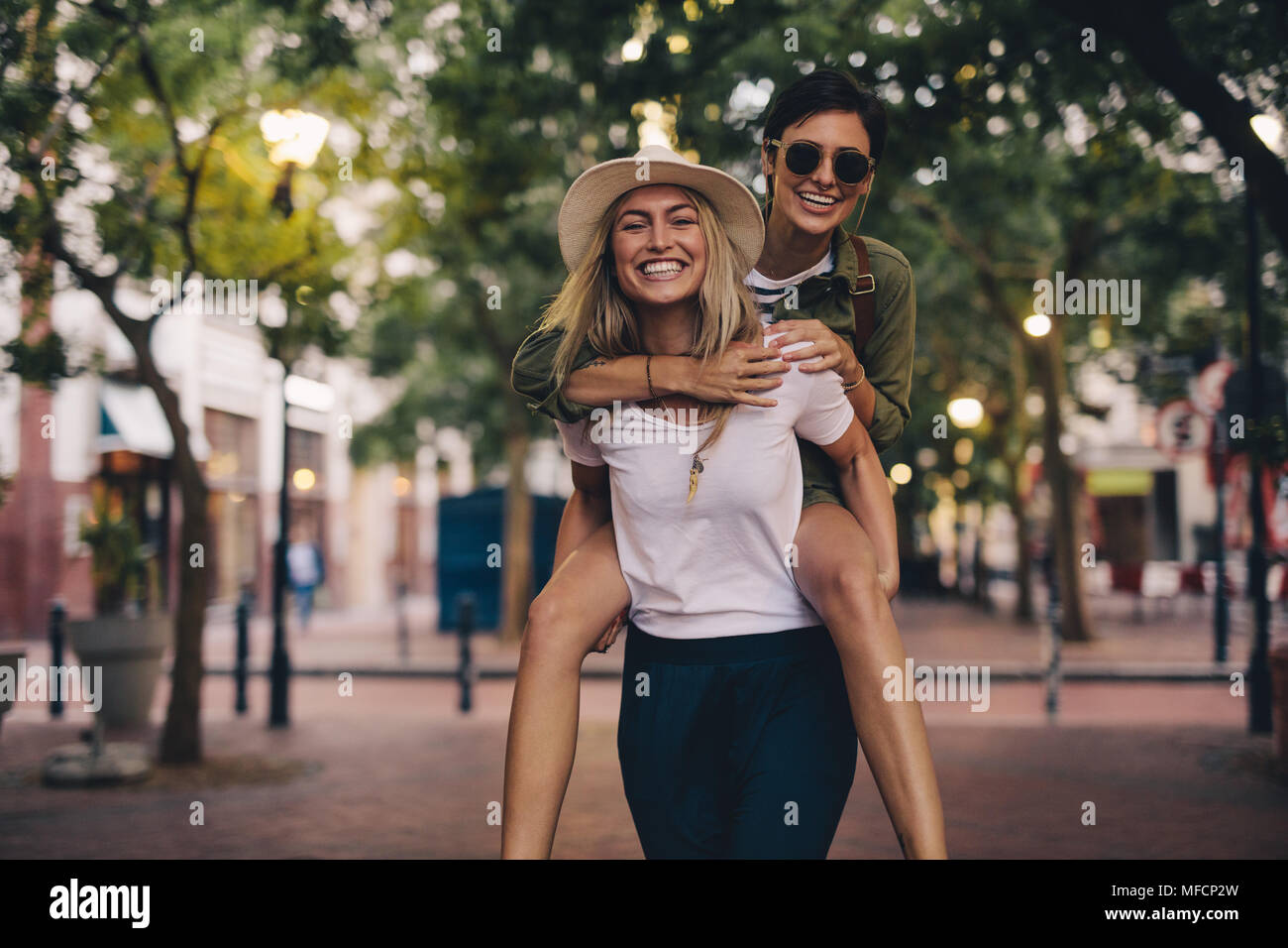 Bella giovane donna che porta il suo amico femmina sul suo retro. Amici di sesso femminile avente il divertimento all'aperto. Foto Stock