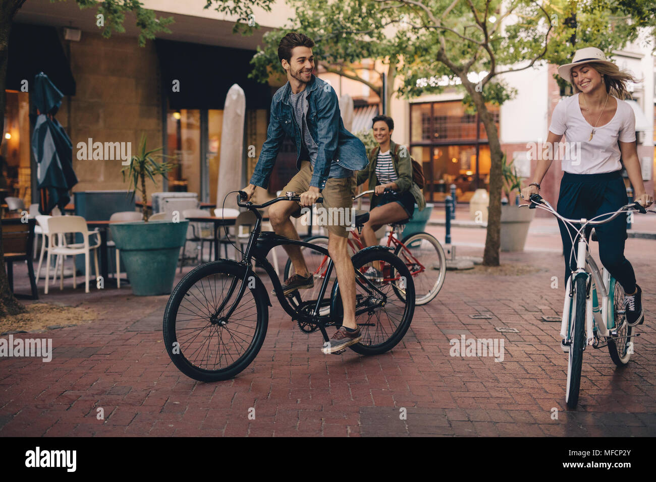 Gli amici con le loro biciclette insieme all'esterno. Giovani uomini e donne equitazione biciclette e divertirsi sulla strada della citta'. Foto Stock