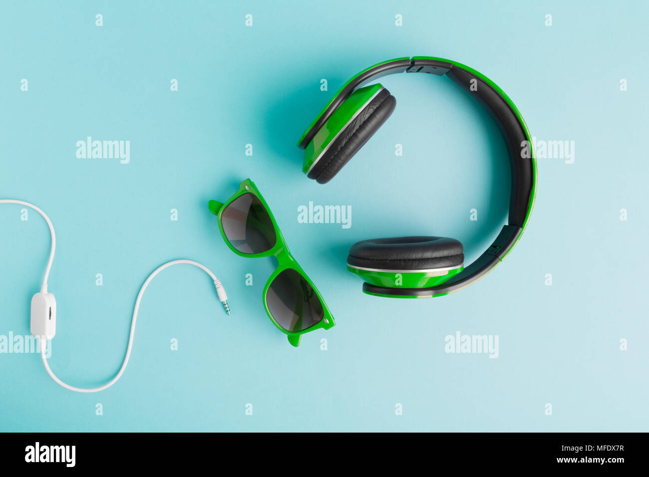 Cuffie verde e occhiali da sole con cavo isolato sul pastello blu sfondo laici piana. Foto Stock