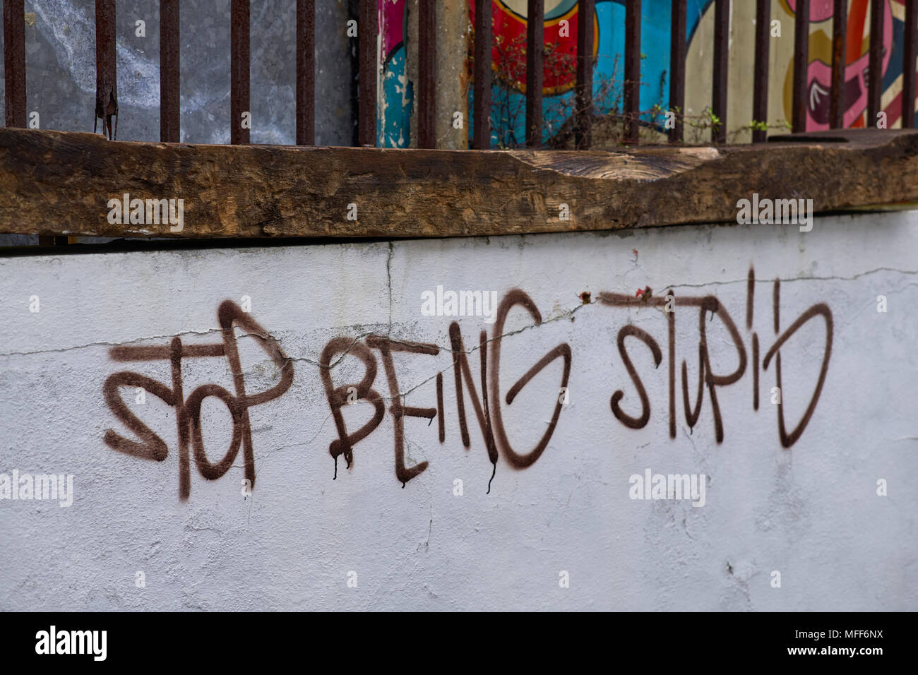 Smettere di essere stupido scritto su un muro bianco marrone con vernice spray Foto Stock