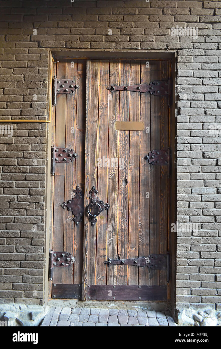 Antica porta di legno in una parete di mattoni con una cerniere forgiato e bloccare Foto Stock