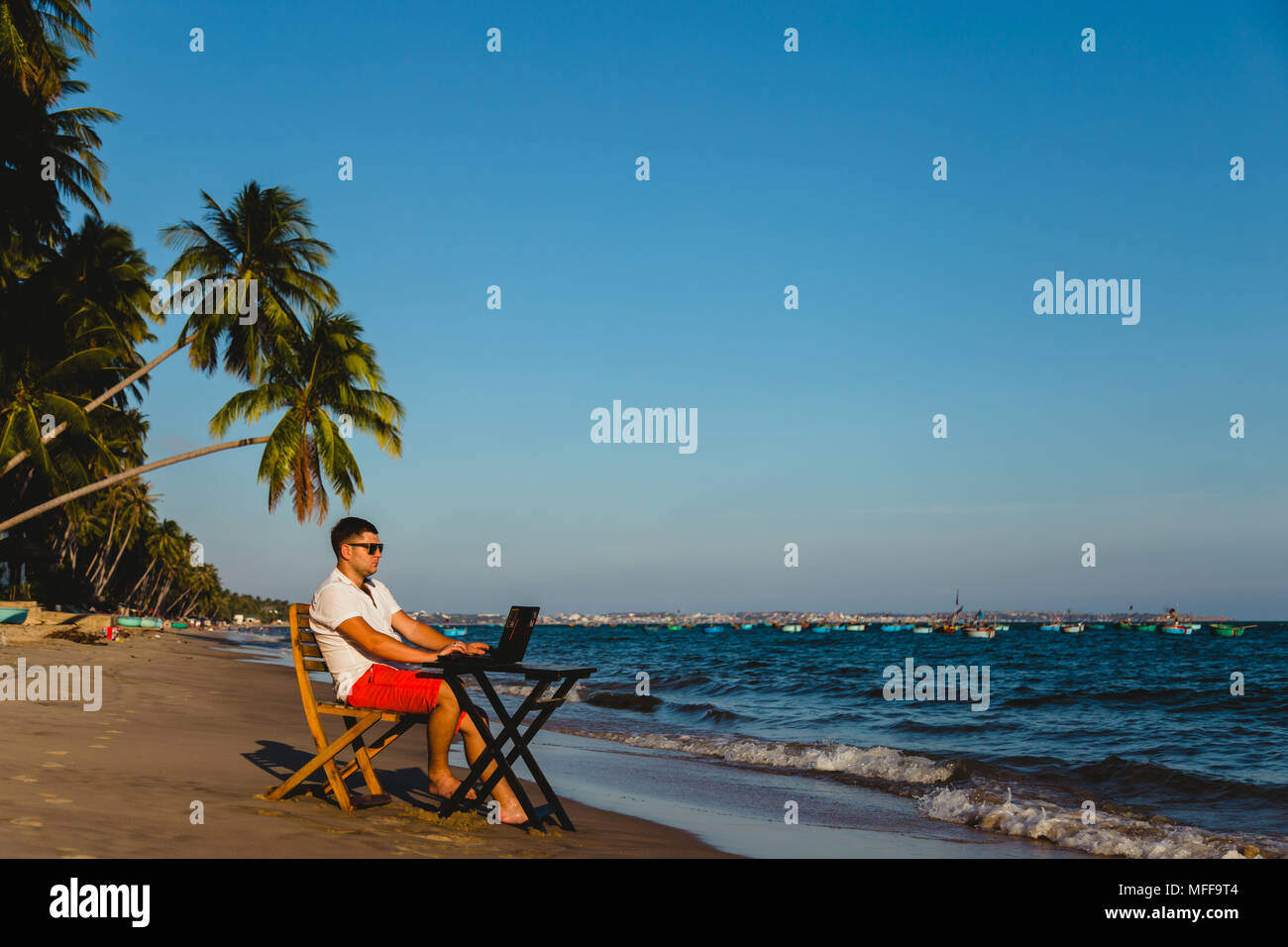 Uomo che lavora con un computer portatile, su un amaca in spiaggia. Concetto di digital nomad, lavoratore remoto, posizione indipendente imprenditore. Foto Stock